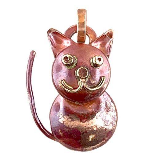 Small chubby cat pendant with red-orange patina and brass accents, handcrafted by Patricia Healey using the repoussé technique.