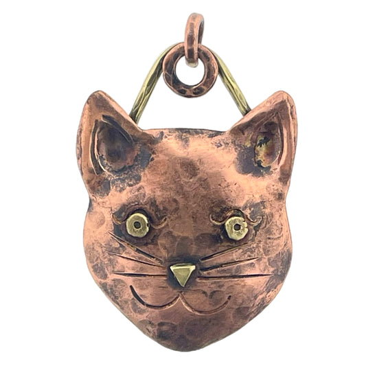 Copper cat face pendant with brass accents, expressive eyes, and warm antique patina, handcrafted by Patricia Healey using repoussé technique.
