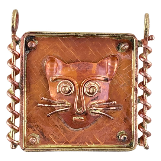 Whimsical copper cat pendant with wide eyes and coiled brass detail, handcrafted by Patricia Healey with a flame patina finish.