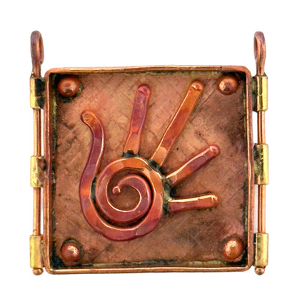 Handmade copper and brass pendant with raised spiral hand design, square shape, flame-heated finish, and textured background.